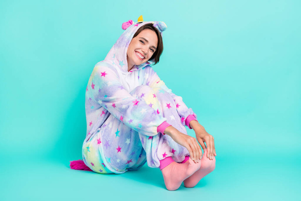 Photo of sweet charming young lady unicorn sleepwear sitting floor smiling isolated turquoise color background. - Fotografie, Obrázek