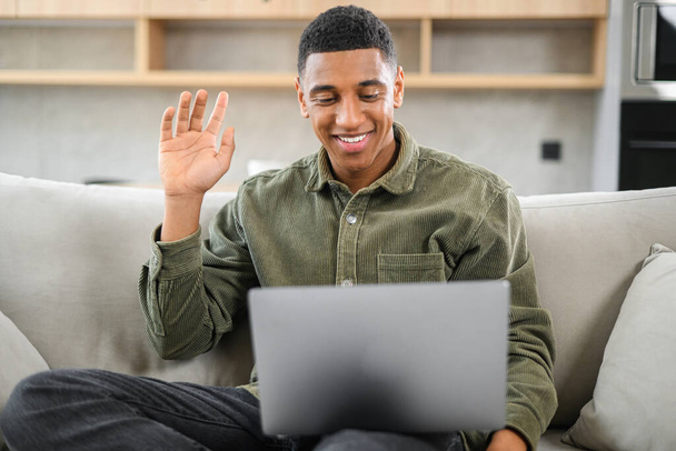 Video call concept. Multiracial freelancer man waving hello into laptop webcam. Black guy connected via video with family, friends or colleagues working remotely from home - Foto, Bild