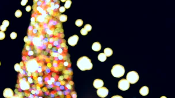 Büyük bir yılbaşı ağacı. Parlak renkli çelenkler ve gece aydınlatmasıyla süslenmiş. Yanıp sönen ışıkları olan Noel ağacı. Arka plan bulanık. Yılbaşı ve Noel tatili - Video, Çekim