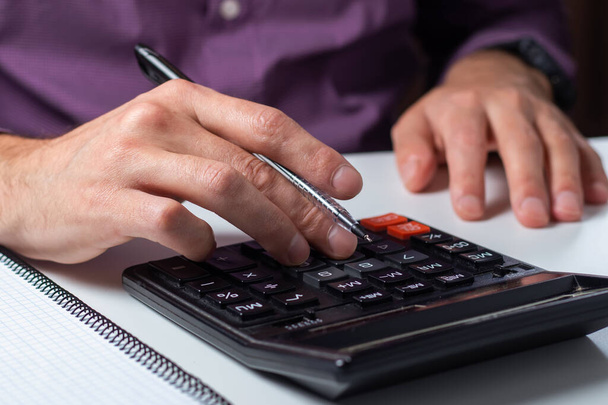 Man 's handen met rekenmachine op kantoor en financiële gegevens analyseren tellen op witte bureau. - Foto, afbeelding