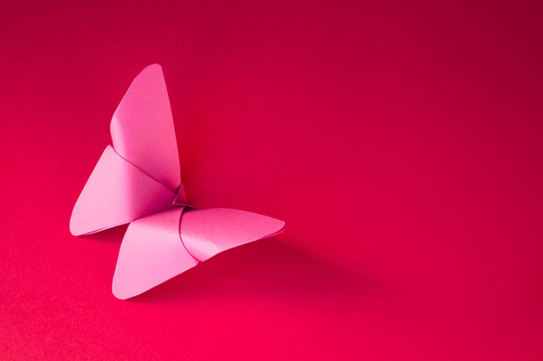 ピンクの紙の蝶の折り紙は、空白の赤い背景に隔離された. - 写真・画像