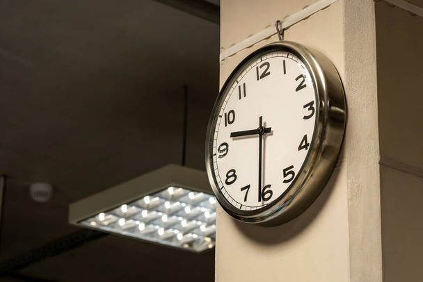 One single simple industrial clock in a factory hall or a corporate office on the wall. Working 9 to 5, clocking in and out, time flow, hourly wage abstract business concept, symbol, nobody, no people - Photo, Image
