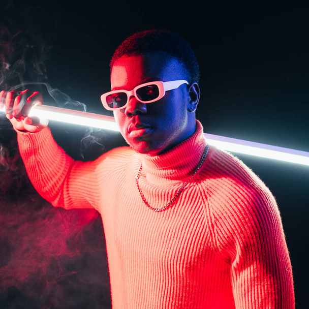 Neon night portrait. Cyberpunk man. Sci-fi character. Serious confident guy holding LED light futuristic sword in smoke at dark studio background. - Foto, afbeelding