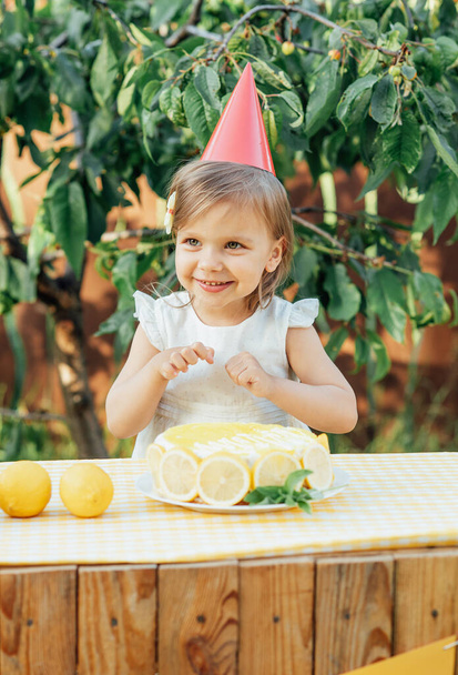 girl eating lemon Birthday cake. Lemonade birthday party at summer park. food, celebration and festive concept. Little child drinks natural lemonade at stand in park - Фото, изображение