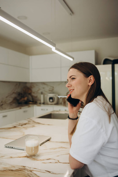 Szczęśliwa kobieta rozmowy na telefon komórkowy podczas gotowania w kuchni. - Zdjęcie, obraz