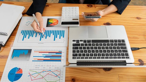 Бизнесмен держит ручку, указывая на маркетинговый график и работая с ноутбуками и финансовыми документами - Фото, изображение
