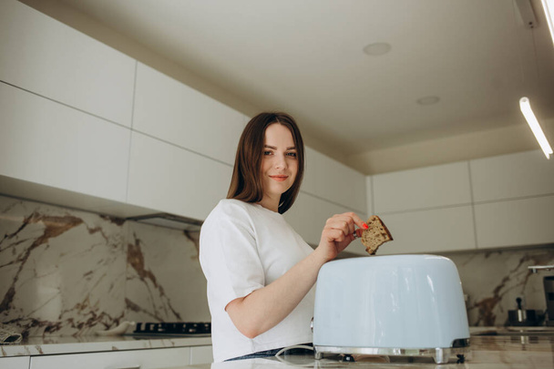 Hübsche junge Frau bereitet zu Hause in der Küche einen Toast zu. Modernes Interieur, Küchenmöbel. Kochen zu Hause. Gesunde Ernährung und Ernährung - Foto, Bild