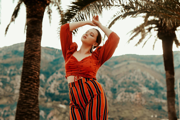 Stilvolle Frau im Sommer vor dem Hintergrund von Palmen und Bergen. Spanierin in rotem Anzug und langen Ohrringen - Foto, Bild