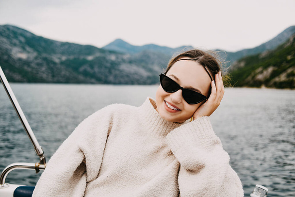 Une fille en lunettes de soleil et un costume blanc montent sur un yacht. Voyage dans les montagnes par la mer. Voyager - Photo, image