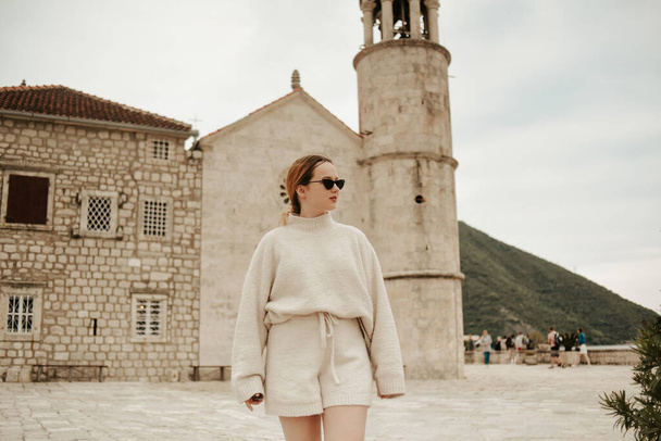 A girl in sunglasses and a white suit walks on the island. Travel, Montenegro. Boka island Church of Our Lady of the Rocks Kotor Bay - Photo, Image