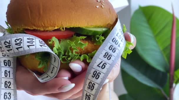Conceito de dieta, mulher segurando hambúrguer de gordura prejudicial com fita métrica branca. - Filmagem, Vídeo