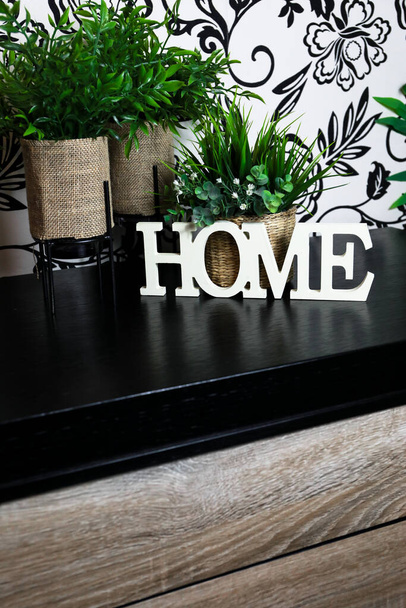 Interieur van een huis, met het woord HOME in het wit op een meubelstuk of tegel en met planten op de rug. - Foto, afbeelding