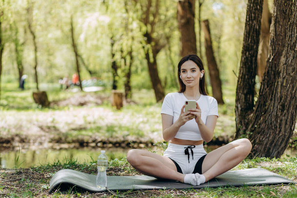 Young smile woman communication mobile phone on nature. Girl using smartphone online internet technology after training fitness in summer park. Tourist relax after exercising sport outdoors - Fotoğraf, Görsel