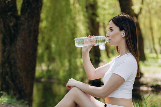 sovi nainen urheilu vaatteet juomaveden treenatessa, jooga puistossa syksyllä aurinkoinen päivä. - Valokuva, kuva