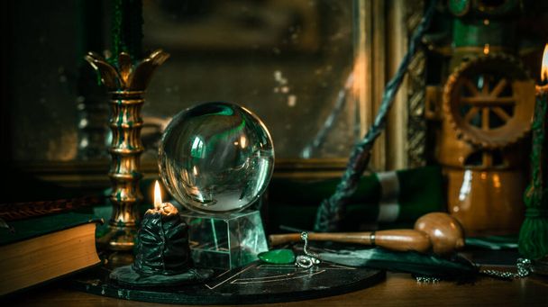 Illustration of magical stuff....candle light, Chrystal ball, magic wand, book of spells dark background, Slytherin school, green aesthetic, Halloween time - Photo, Image