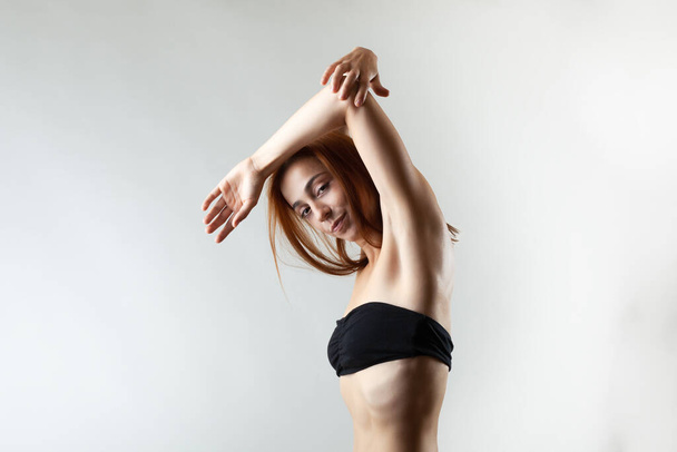 Beautiful girl with burnt orange hair stretching and making ballet pose. Studio portrait on gray background. - Φωτογραφία, εικόνα