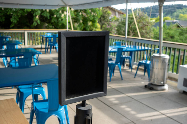 Selective focus on an empty black sign in front of a reserved seating area filled with blue chairs under an outdoor canopy - Photo, Image