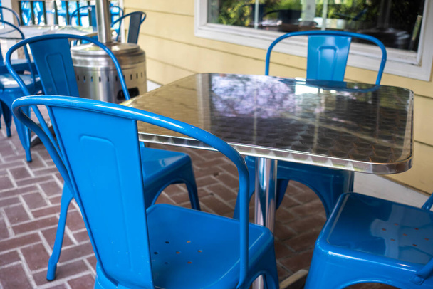 Colorful view of bright blue chairs gathered around a reflective metal table on an outdoor patio at a restaurant - Photo, Image