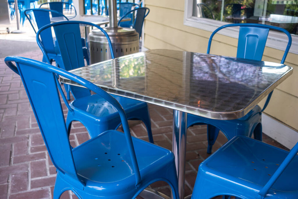 レストランの屋外パティオの反射金属テーブルの周りに集まった明るい青の椅子のカラフルな景色 - 写真・画像