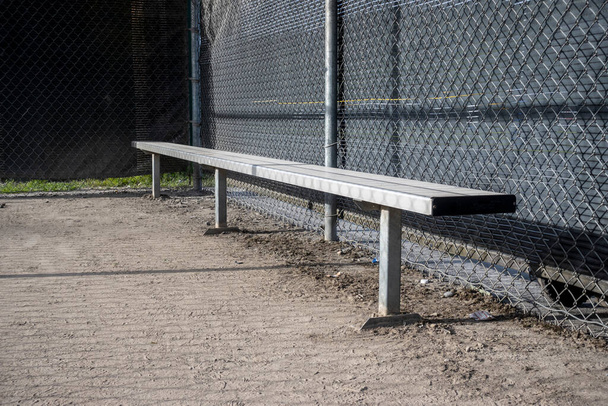 Angled view of a metal bench inside a baseball dugout at a sports field - Photo, Image