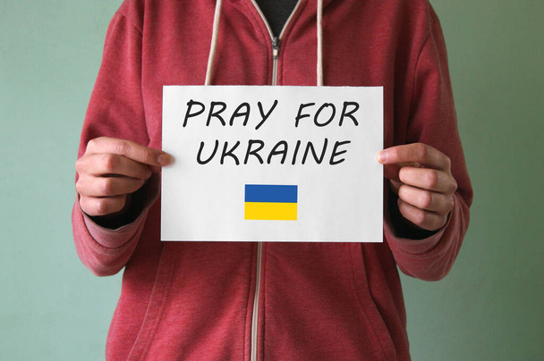 Een jongeman heeft een blad met de inscriptie PRAY FOR UKRAINE. Oorlog in Oekraïne. Stop de oorlog.. - Foto, afbeelding