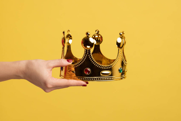 Closeup of woman hand holding golden crown, concept of awards ceremony, privileged status, superior position. Indoor studio shot isolated on yellow background. - 写真・画像