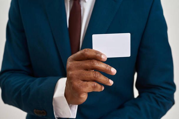 Selective focus close up of business card in hand of african american entrepreneur or ceo manager. partial image of man wearing suit. Concept of modern successful male lifestyle - Foto, Bild