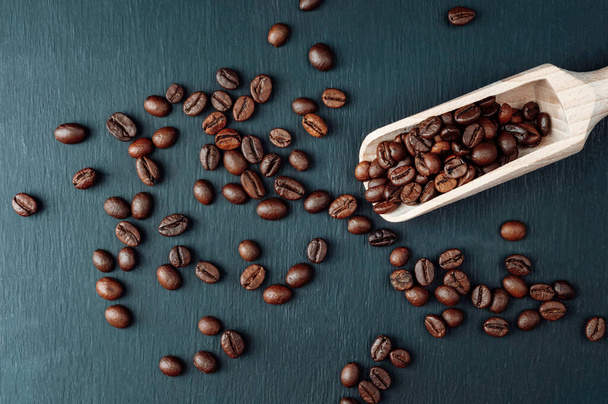 Kaffeebohnen und Holzlöffel vorhanden. Kaffeebohnen auf einem dunklen. Konzept: Export und Import von Kaffeebohnen, Kaffeekonsum. verstreute frisch geröstete Kaffeekörner mit Kopierfläche für Werbung - Foto, Bild