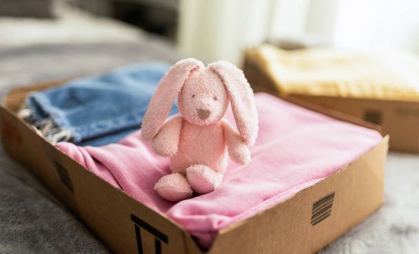 Stack clothing for sorting and donation in cardboard boxes with toy bunny for kids. Clothes for charity. Folding clothing storage. Environmentally Friendly Consumption. - Zdjęcie, obraz