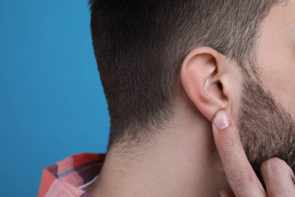 Man pointing at his ear on light blue background, closeup - Foto, Bild