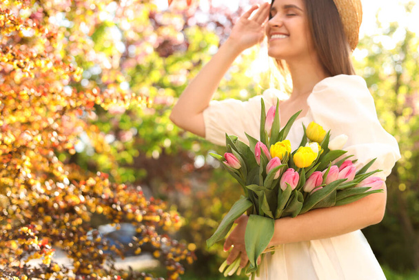 Beautiful young woman with bouquet of tulips in park, focus on flowers. Space for text - Foto, Imagem