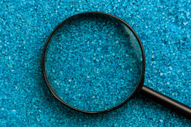 Magnifying glass on the background of sea aromatic bath salts. Concept of searching for romantic pleasure. Abstract copy space - Foto, afbeelding