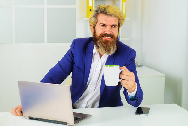 Obchodník pracující s laptopem v kanceláři si dává pauzu na kávu. Podnikatel s šálkem cappuccino - Fotografie, Obrázek