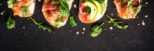 Open sandwiches set with cream cheese, prosciutto, salmon, avocado and fresh greens and vegetables. Long banner format. - Φωτογραφία, εικόνα