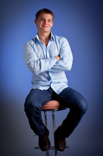 Young man sitting on bar chair with crossed arms - Фото, зображення