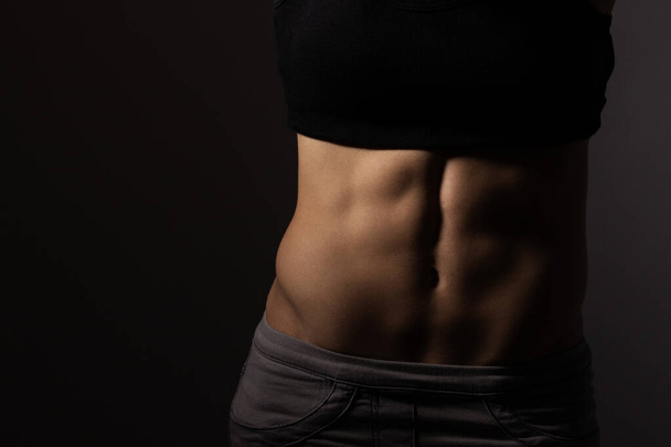 Strong fit woman showing her abs, unrecognizable, dark background - Φωτογραφία, εικόνα
