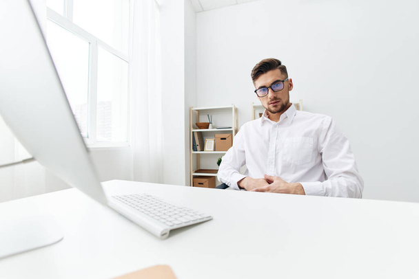 Manager in weißem Hemd sitzt an einem Computer mit einem Handy. Hochwertiges Foto - Foto, Bild