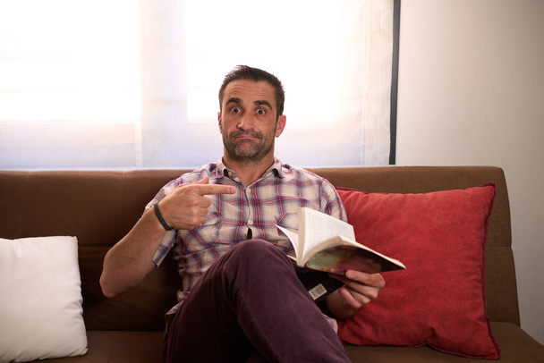 Hombre con camisa a cuadros y libro en la mano sentado relajado en un sofá. Foto de alta calidad - Foto, Imagen