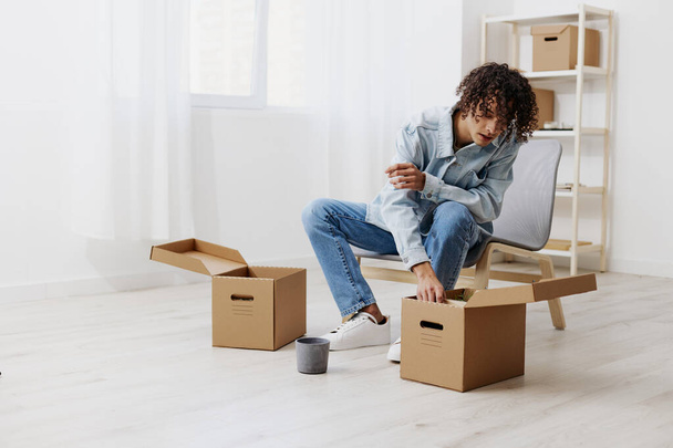 guy with curly hair cardboard boxes in the room unpacking interior. High quality photo - Photo, Image