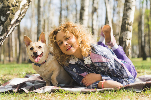 Happy dog and his young caucasian femal owner laying on a checked blanket, smiling at the camera and having fun. High quality photo - Photo, Image
