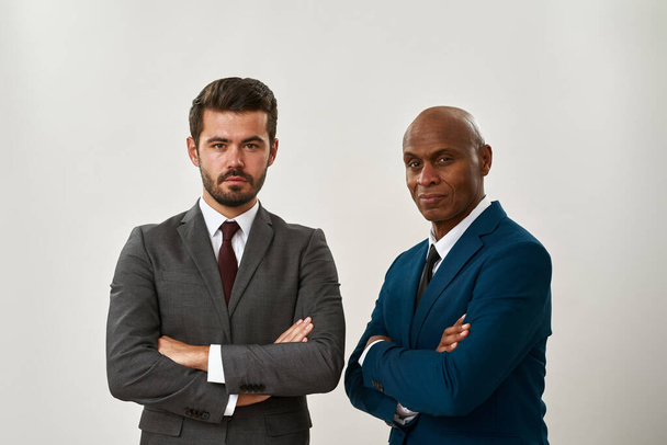 Two confident multiethnic entrepreneurs with crossed arms looking at camera. Men wearing formal wear. Modern successful male lifestyle. Teamwork. Isolated on white background. Studio shoot. Copy space - Foto, afbeelding