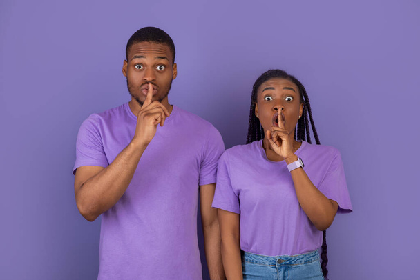 Shh, Keep Silence Concept. Emotional Black Couple Gesturing Hush Sign Posing Standing Isolated Over Purple Violet Studio Wall, Looking Staring At Camera. Holding Finger On Lips, Silent Gesture, Secret - Photo, Image