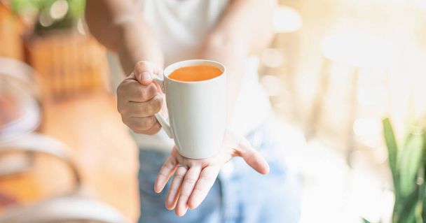 Eine Frau hält eine Tasse Tee in der Hand, während sie im Wohnzimmer sitzt und es sich gemütlich macht. Und Kopierraum. - Foto, Bild