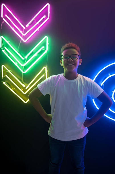 Front view of a cheerful teenager in stylish eyeglasses posing for the camera in a nightclub - Foto, afbeelding