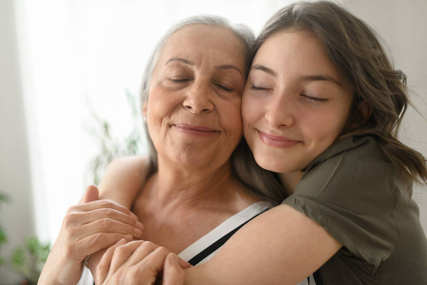 A senior grandmother with teenage granddaguhter hugging together at home. - Fotoğraf, Görsel