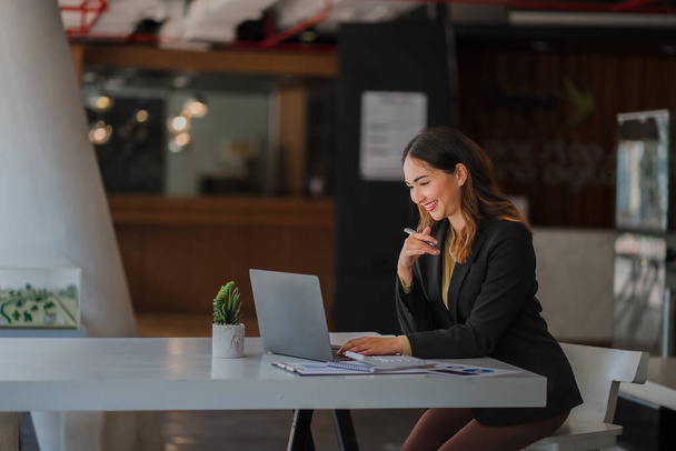 Uśmiechnięta piękna azjatycka bizneswoman siedząca z laptopem i komputerem pracującym nad papierkową robotą zrobić raport analizy konta nieruchomości informacje inwestycyjne finansowe i podatkowe koncepcje systemu - Zdjęcie, obraz