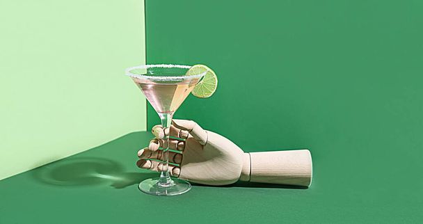 Деревянная рука со стаканом вкусного космополитического коктейля на зеленом фоне - Фото, изображение