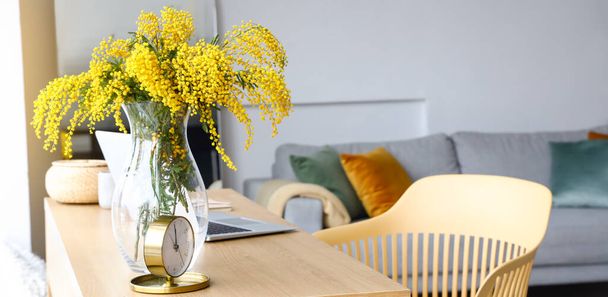 Jarrón con flores mimosa y reloj despertador en la mesa en el interior de la habitación - Foto, Imagen