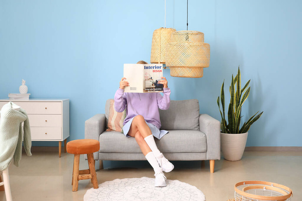 Giovane donna che legge rivista su comodo divano vicino alla parete blu - Foto, immagini