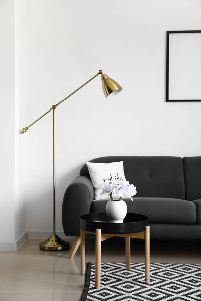 Удобный диван и современная лампа возле белой стены - Фото, изображение